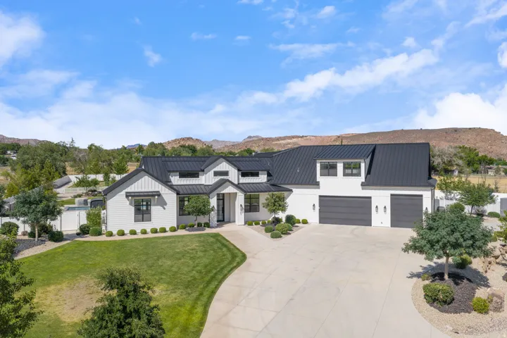 Modern farmhouse residence showcasing a clean-lined white exterior with black metal roof accents, dual garage with white paneling, and architectural detailing including gabled rooflines and substantial driveway