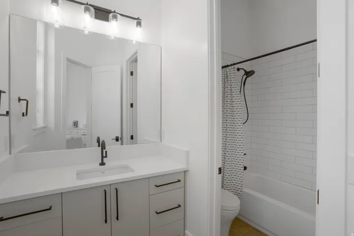 Modern primary bathroom featuring a dual-sink vanity with white quartz countertop, soft-close cabinetry with matte black hardware, and an illuminated mirror with integrated lighting