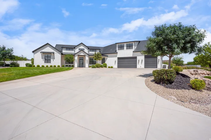 Striking Contemporary Residence featuring a Spacious Concrete Driveway, Dual-Bay Garage with Dark Finishes, Manicured Lawn with Mature Landscaping, Architectural Stone Hardscaping with Native Plantings, and Clean-lined Exterior Elevation with Peaked Roofl