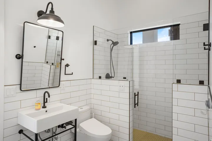 Bathroom featuring white subway tile walls, a wall-mounted rectangular sink with a matte black faucet, and a black-framed mirror