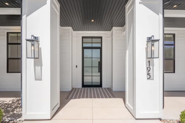 Modern farmhouse entry featuring a covered portico with symmetrical white columns and black-framed glass door