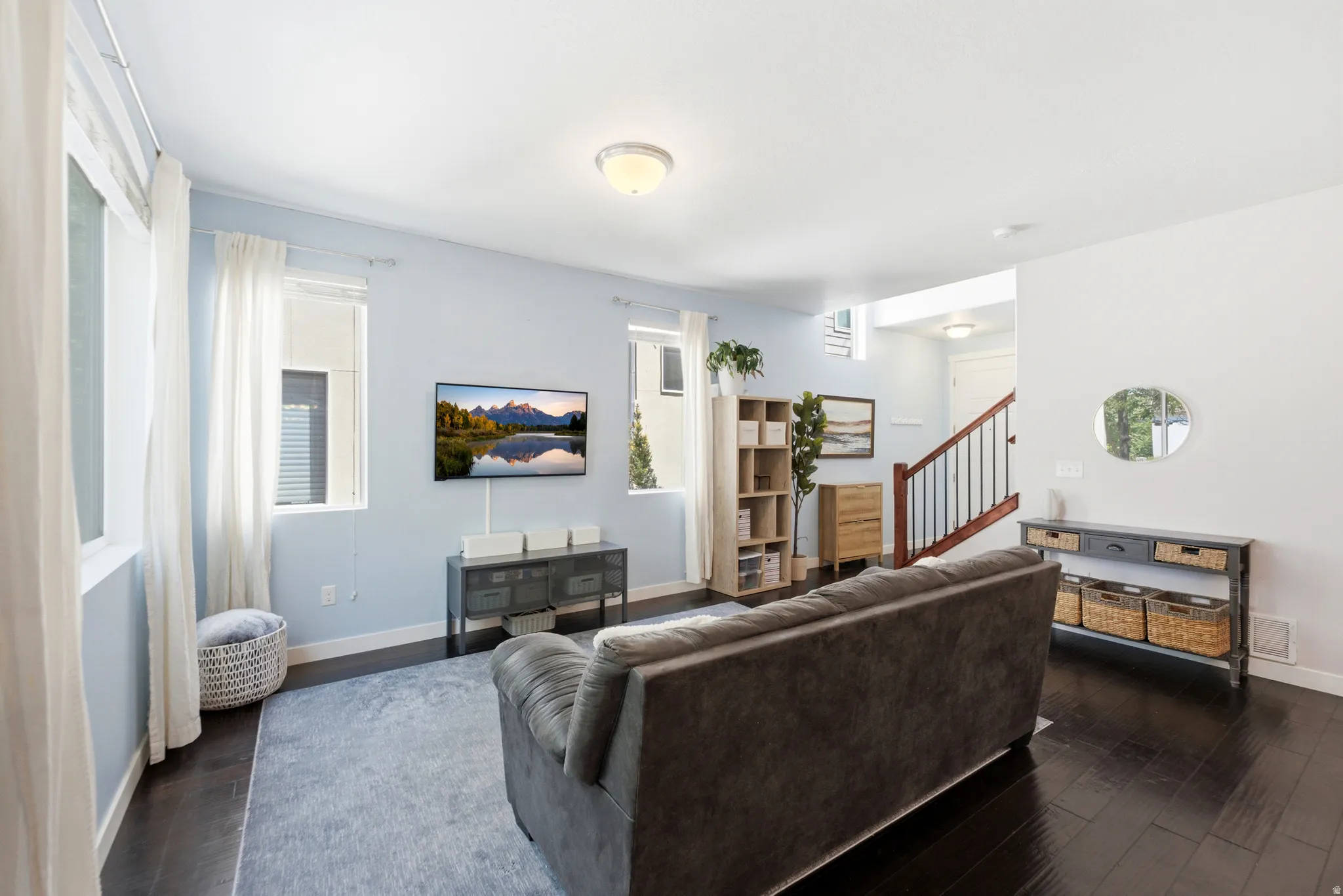 Spacious room featuring dark wood-finish flooring, multiple windows, and a prominent staircase with dark wood handrails and white balusters