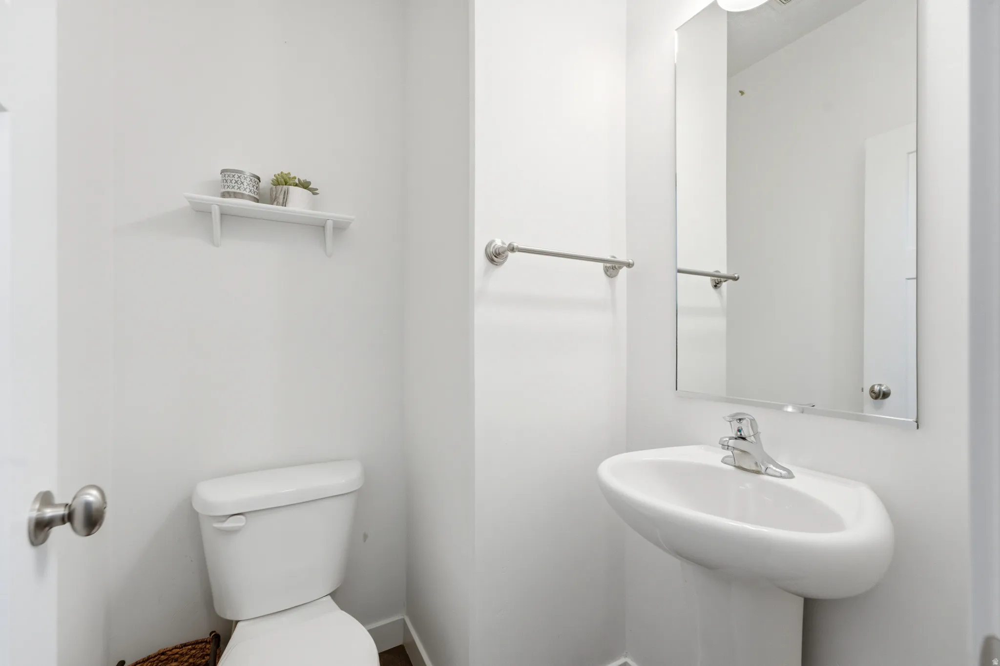 Clean and functional half bath featuring a white ceramic pedestal sink with chrome faucet, toilet with lid, large wall-mounted mirror with chrome hardware, and brushed nickel towel bar