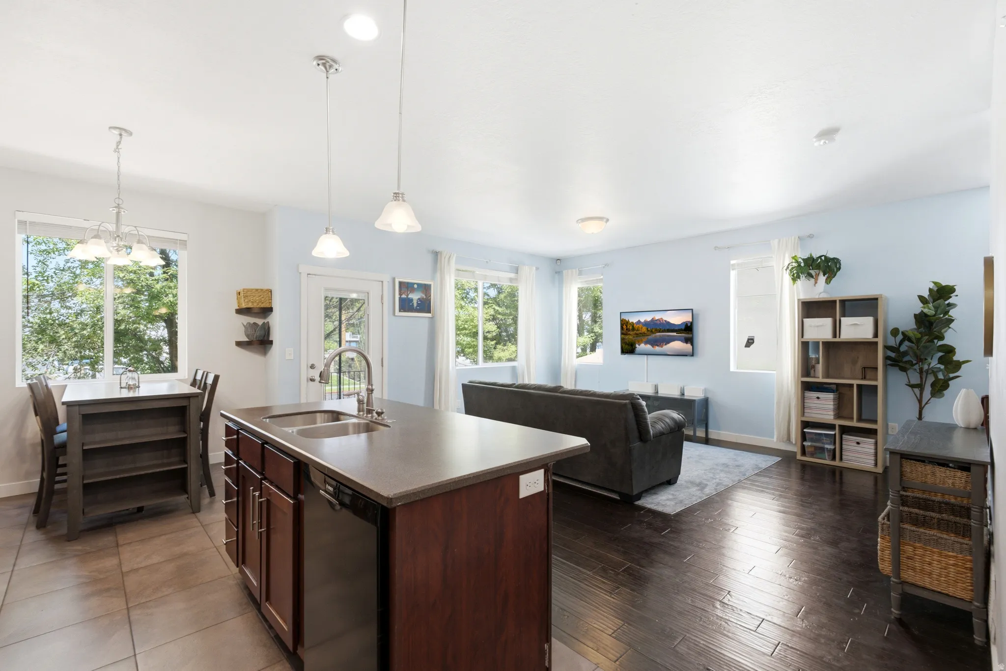 Open-concept living space featuring a large kitchen island with dark wood cabinetry and stainless steel countertop, pendant lighting, and hardwood flooring throughout