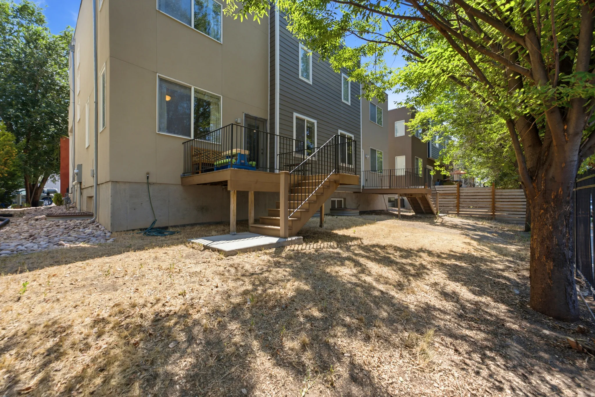 Spacious backyard oasis featuring a custom wood-frame deck with metal railings, mature shade trees, and level gravel landscaping