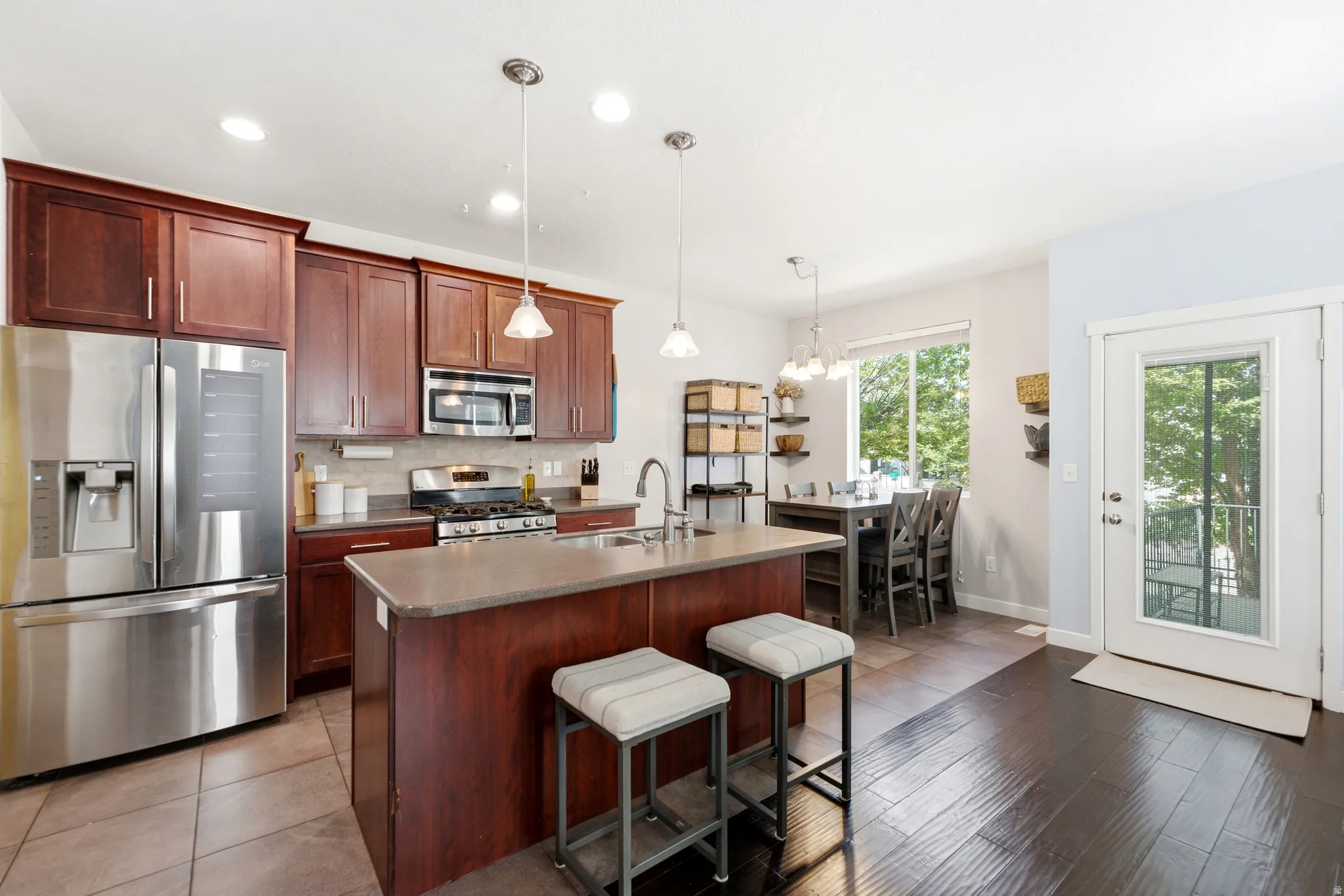 Kitchen featuring stainless steel appliances, rich wood cabinetry, a center island with pendant lighting, and tile flooring