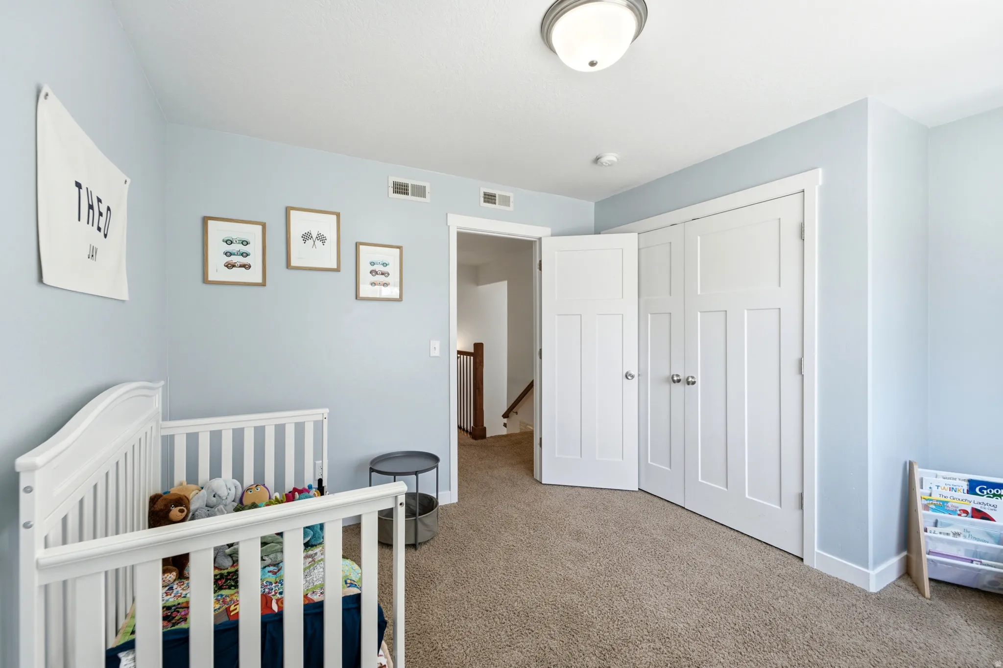Bright nursery featuring soft blue walls, white six-panel closet doors, neutral carpet flooring, and ample natural light from recessed ceiling fixtures
