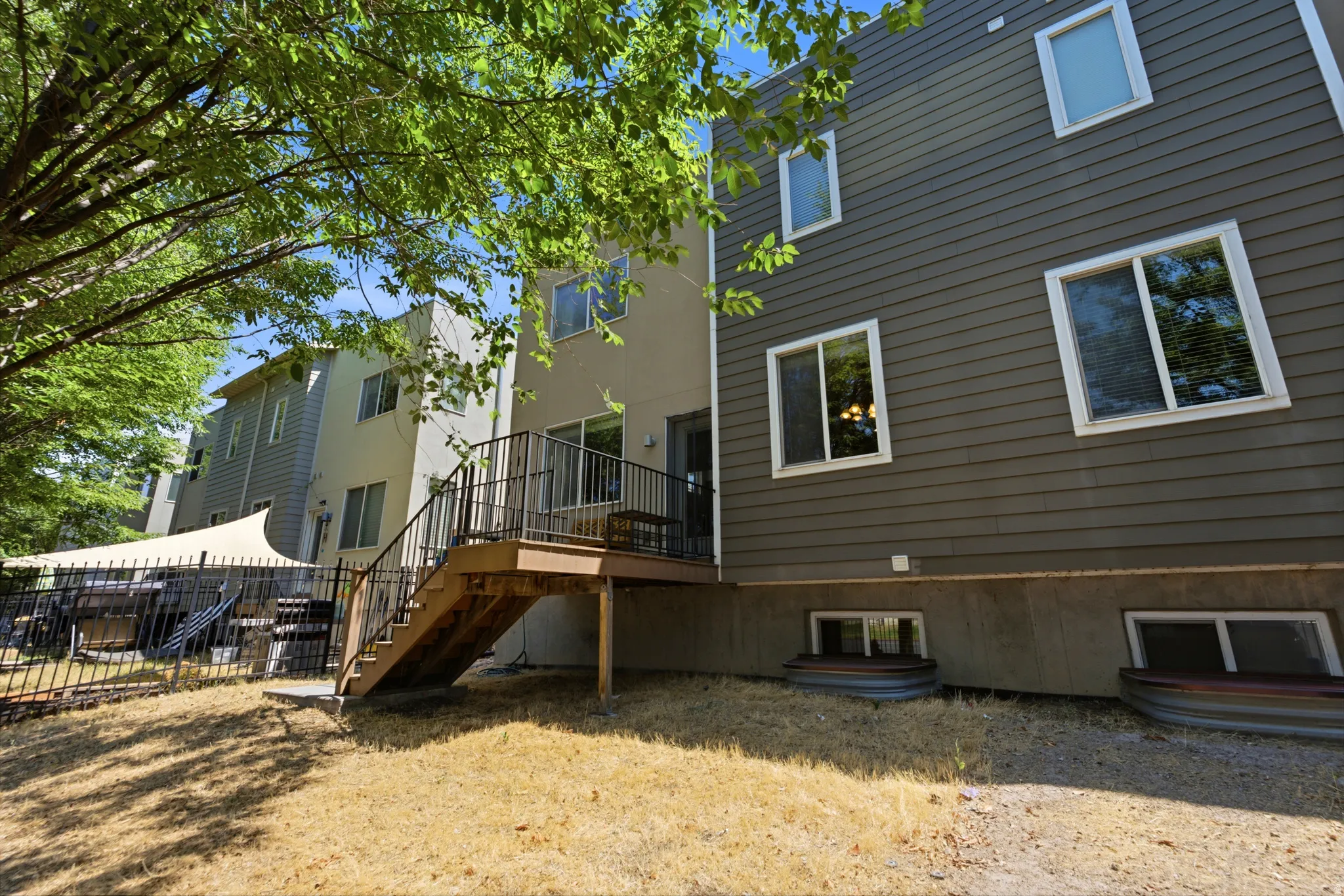 Rear exterior featuring a multi-level wood deck with black metal railings, leading to a fenced backyard area