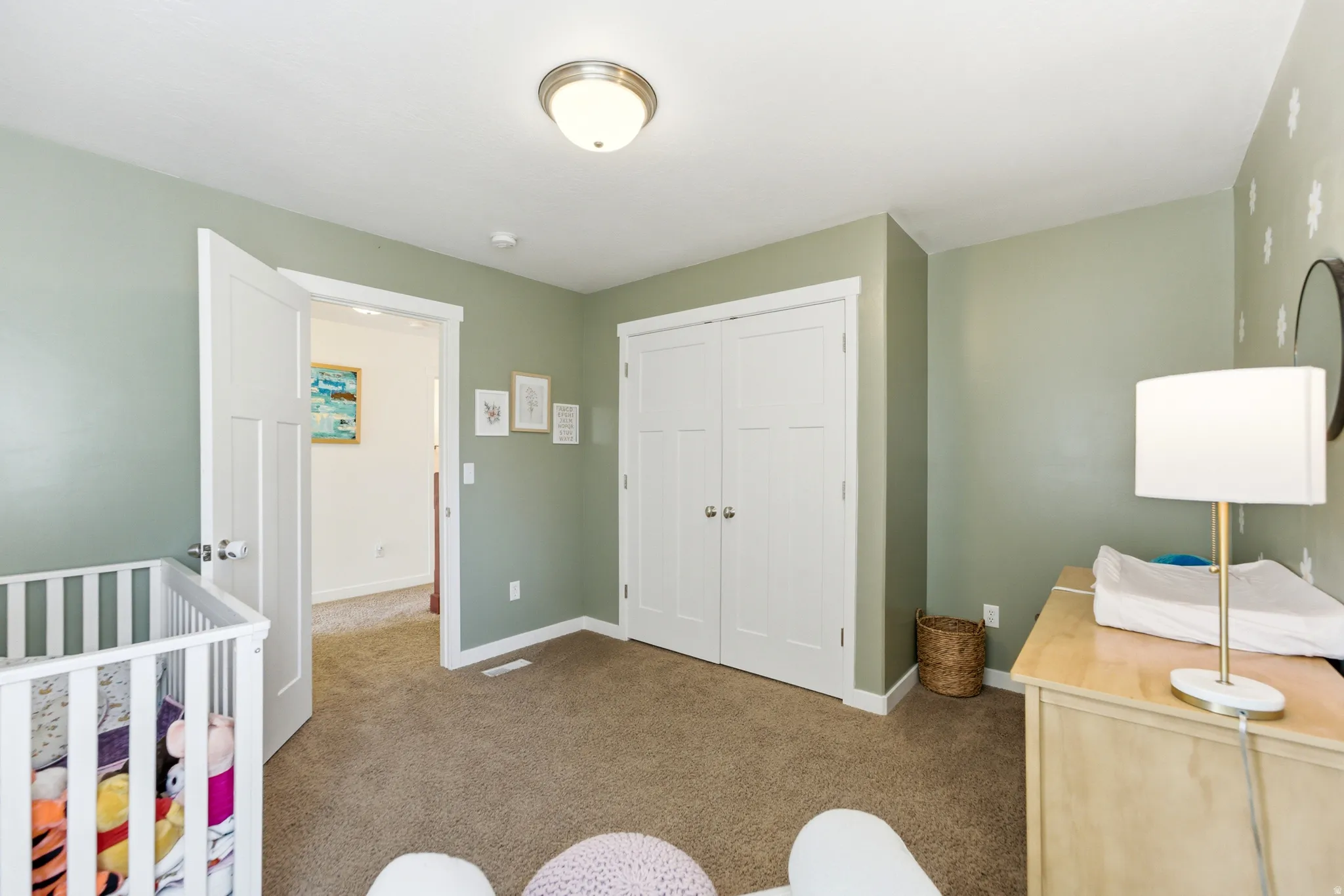 Bright nursery featuring sage-green walls, white six-panel closet doors, neutral carpet flooring, and recessed ceiling lighting