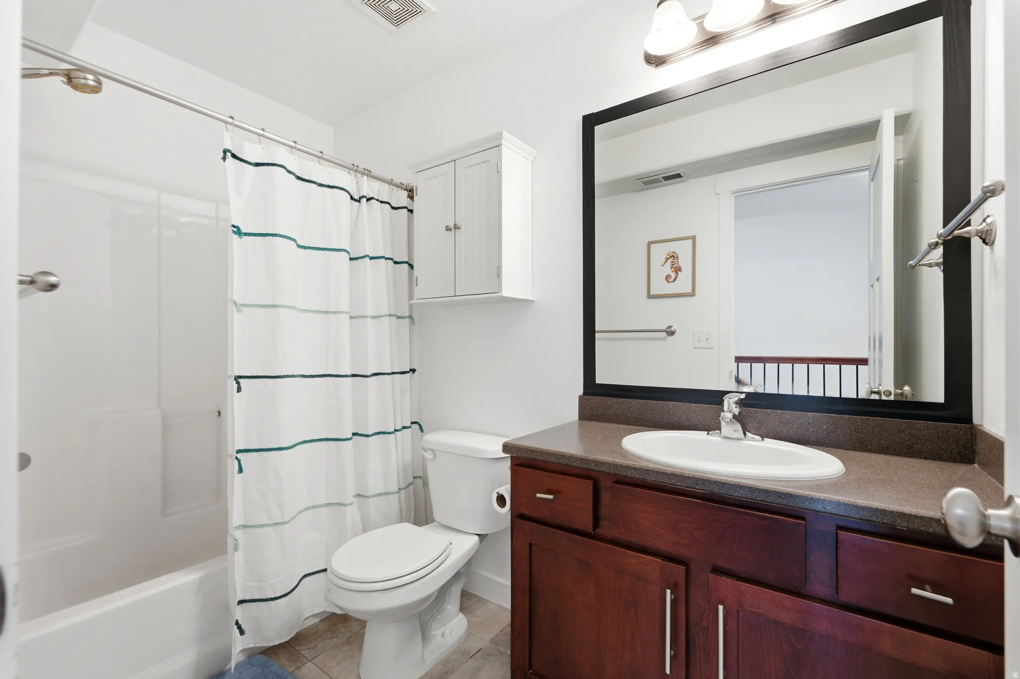 Spa-inspired bathroom featuring a rich wood-finish vanity with dual sink configuration, ample storage cabinetry, and a large framed mirror with integrated lighting