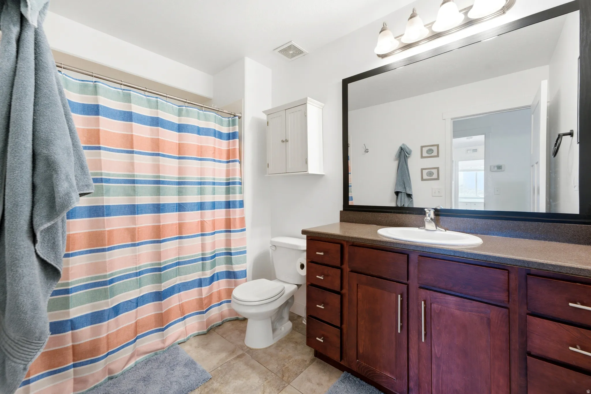 Spa-inspired primary bathroom showcasing a rich wood-finish vanity with dual sinks, ample storage cabinetry, and a framed mirror with integrated lighting