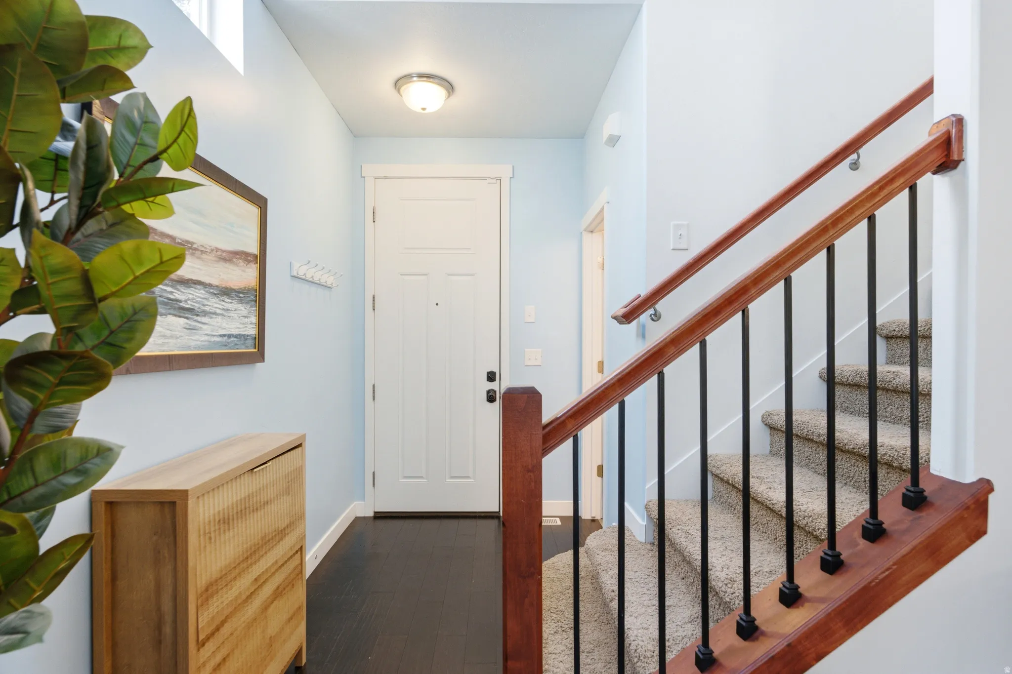 Welcoming entryway featuring a light blue accent wall, wood-finish cabinetry with cane detailing, and a striking staircase with a rich wood handrail and black metal balusters