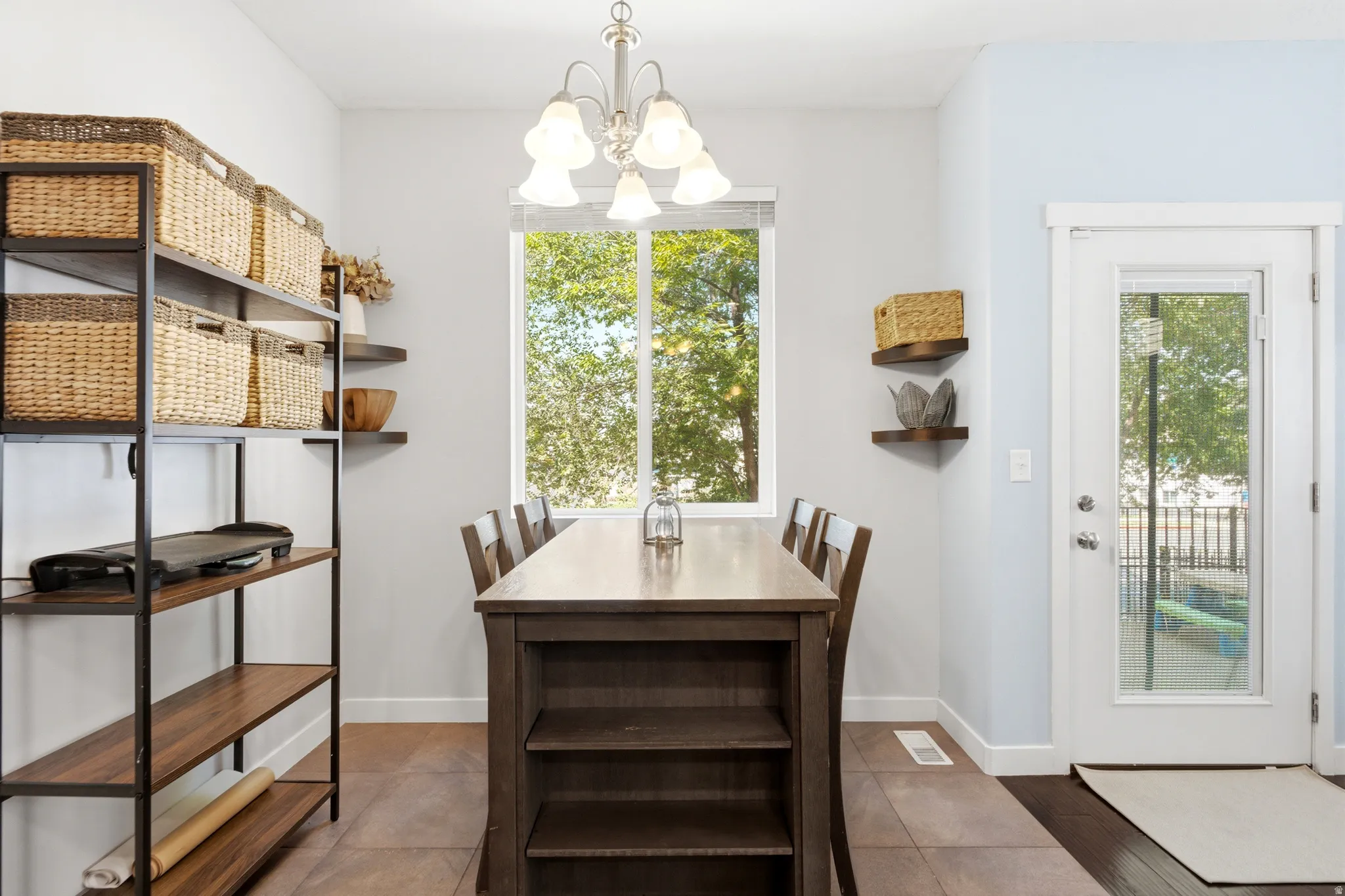 Bright dining room featuring a wood-finish table with built-in shelving, pendant lighting, and French doors opening to outdoor space