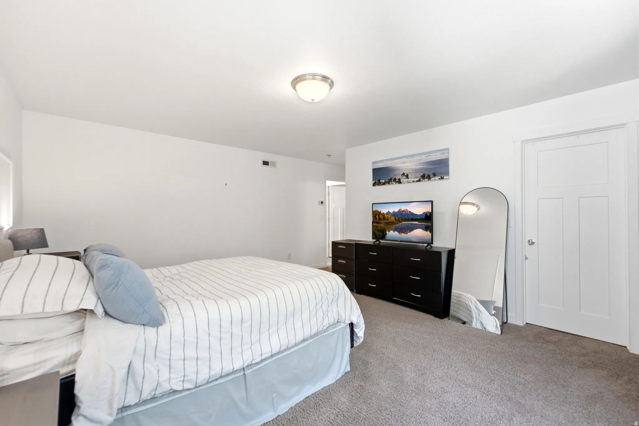 Spacious bedroom featuring neutral carpeting, a ceiling-mounted light fixture, and ample natural light
