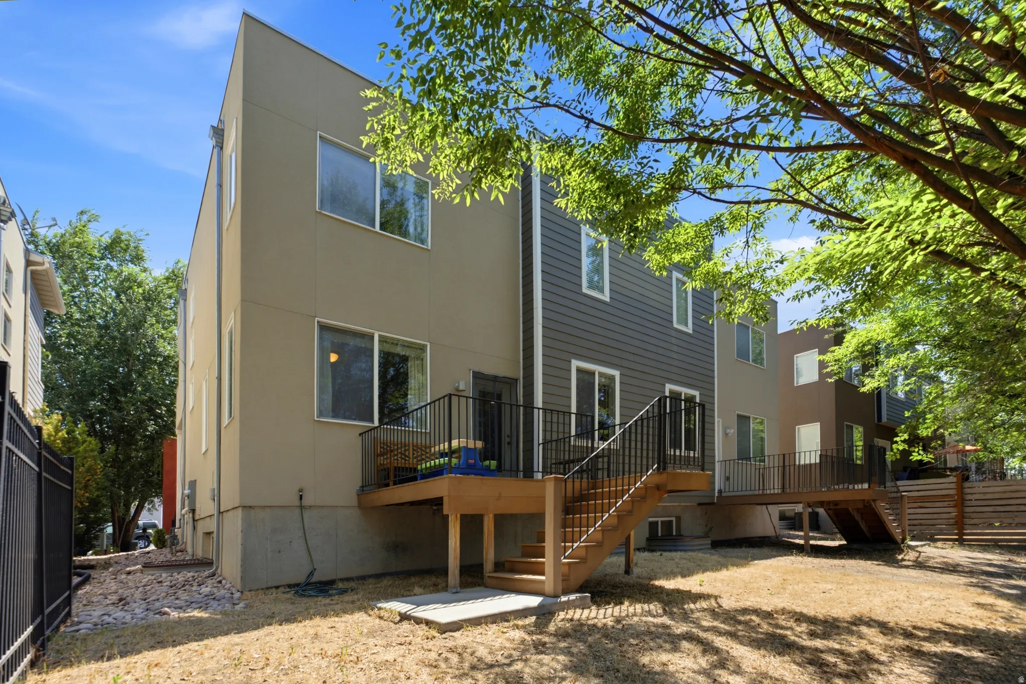 Rear exterior showcasing a multi-level deck with black metal railings, a sliding glass door, and a ground-level concrete patio