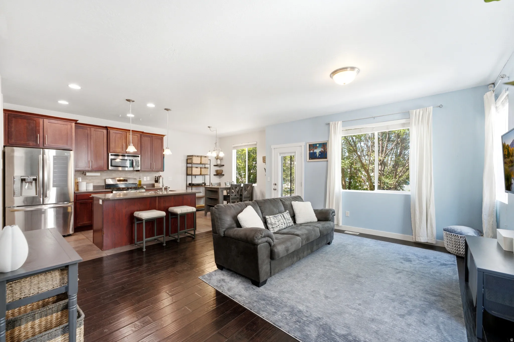 Open-concept living space featuring a dark wood-finish floor throughout, complemented by light blue accent walls and abundant natural light from multiple windows