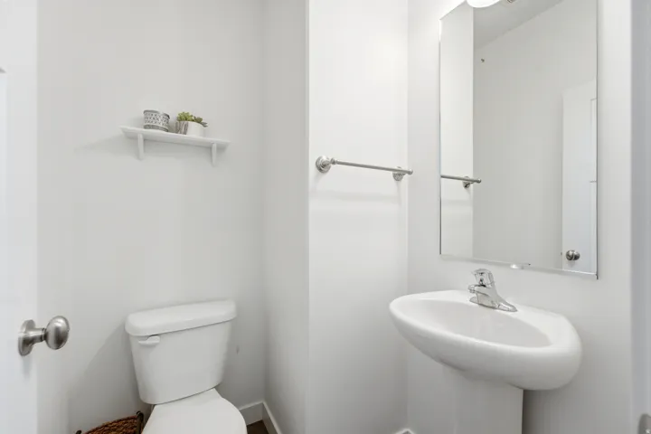 Clean and functional half bath featuring a white ceramic pedestal sink with chrome faucet, toilet with lid, large wall-mounted mirror with chrome hardware, and brushed nickel towel bar