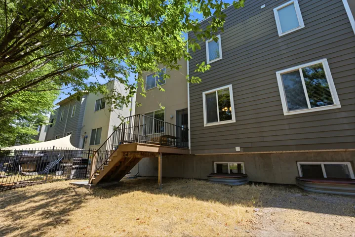 Rear exterior featuring a multi-level wood deck with black metal railings, leading to a fenced backyard area