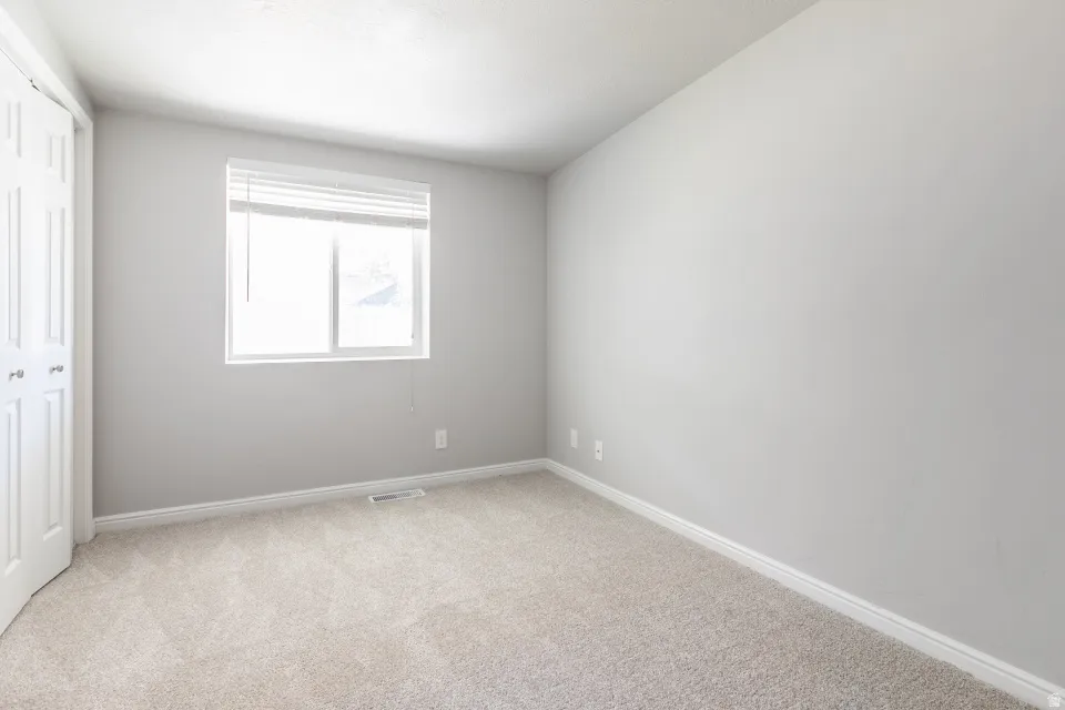 Bright, light-filled bedroom with neutral gray walls, neutral carpet flooring, and a large window with natural light