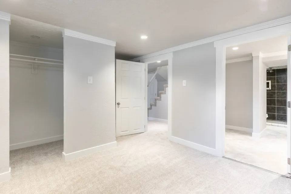 Spacious primary suite featuring dual walk-in closets with glass-front doors, neutral wall finishes, recessed ceiling lighting, and direct access to an ensuite bathroom with tile shower enclosure and dark tile accents