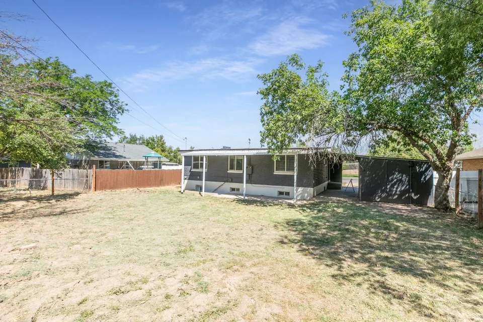 Expansive backyard featuring a partial privacy fence, mature trees, and a detached shed