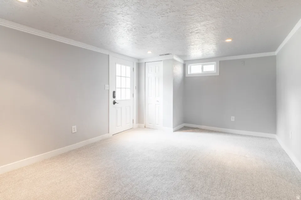 Light gray carpeting in a room featuring a white paneled door with windowpanes, a recessed window, and white trim