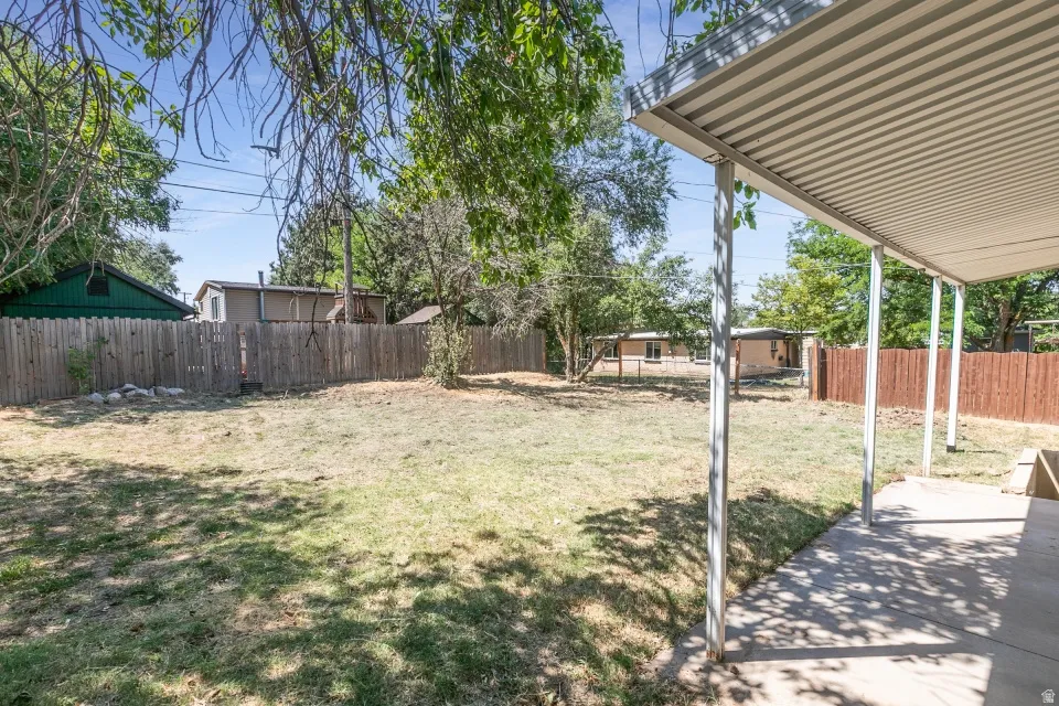 Spacious backyard with mature shade trees, level lawn, and covered patio structure with metal posts and corrugated roof