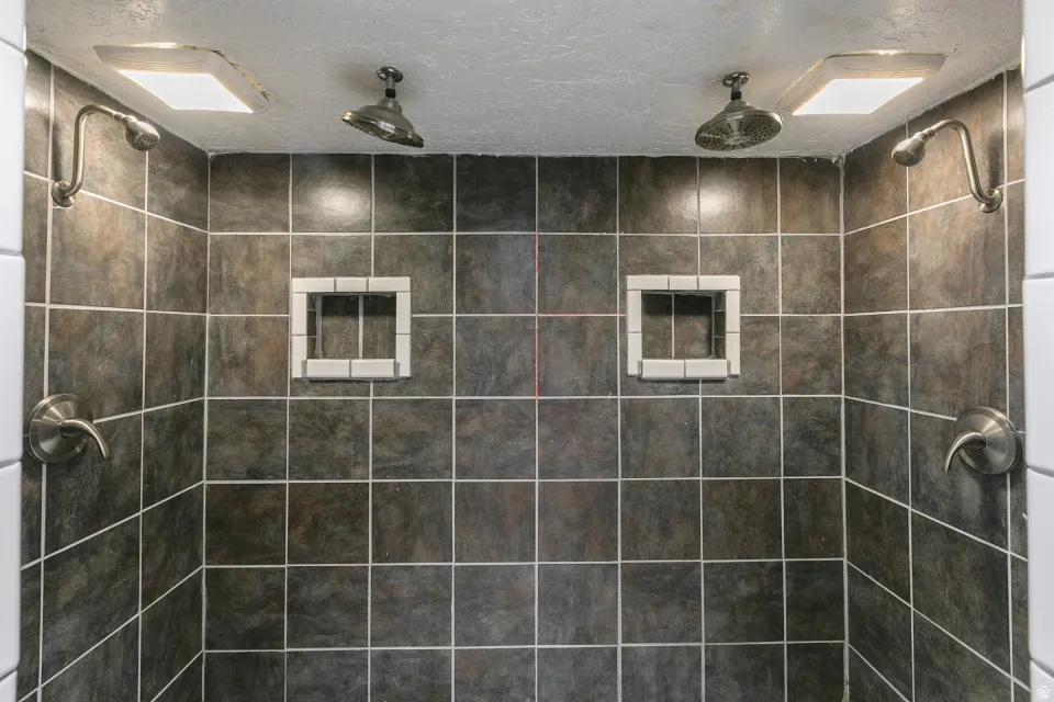 Luxurious dual-head walk-in shower featuring large-format charcoal tile walls with contrasting grout lines, two recessed niches with white tile framing for storage and organization, and dual rainfall showerheads mounted on the ceiling for an spa-like bath