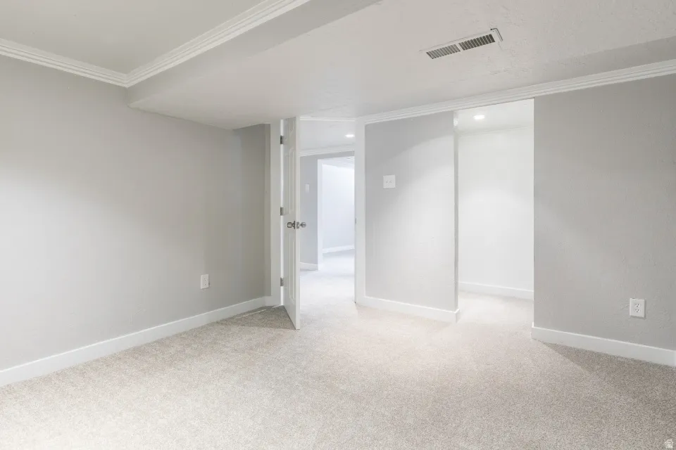 Carpeted room featuring light gray walls, white baseboards, and crown molding