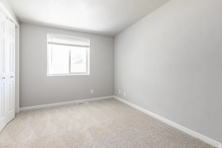Bright, light-filled bedroom with neutral gray walls, neutral carpet flooring, and a large window with natural light