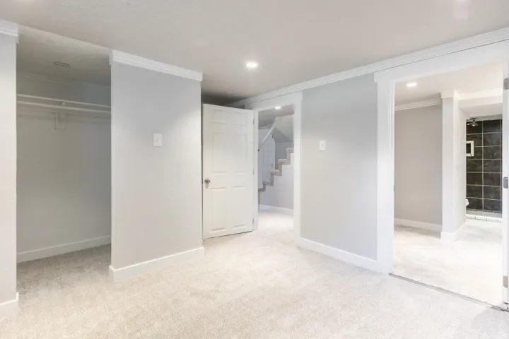 Spacious primary suite featuring dual walk-in closets with glass-front doors, neutral wall finishes, recessed ceiling lighting, and direct access to an ensuite bathroom with tile shower enclosure and dark tile accents