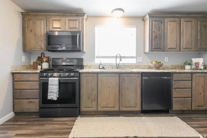 Kitchen featuring wood-finish cabinetry, granite-style countertops, stainless steel sink with gooseneck faucet, black appliances including oven range, microwave, and dishwasher, and wood-finish flooring