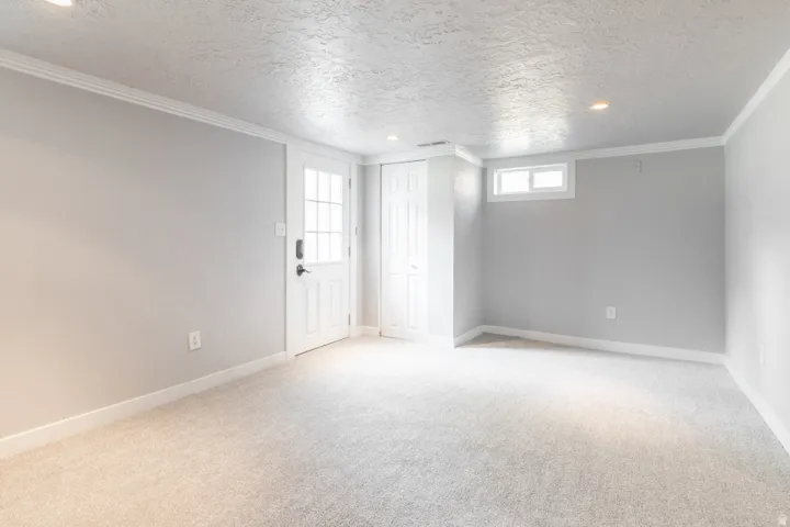 Light gray carpeting in a room featuring a white paneled door with windowpanes, a recessed window, and white trim