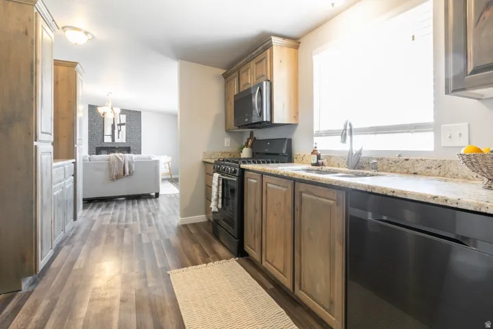 Galley-style kitchen featuring wood-finish cabinetry, granite countertops, stainless steel appliances including a gas range and dishwasher, undermount sink with chrome faucet, and wood-finish flooring that extends throughout the home