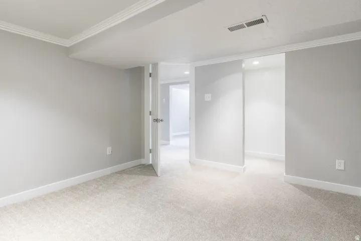 Carpeted room featuring light gray walls, white baseboards, and crown molding