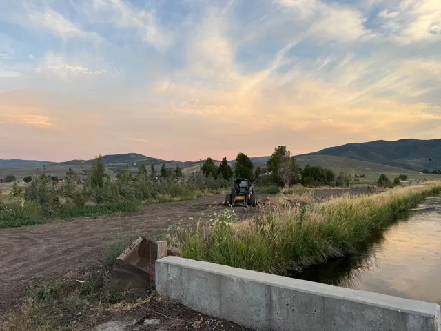 Irrigated acreage featuring a concrete water conveyance system, mature riparian vegetation, and rolling hillside backdrop