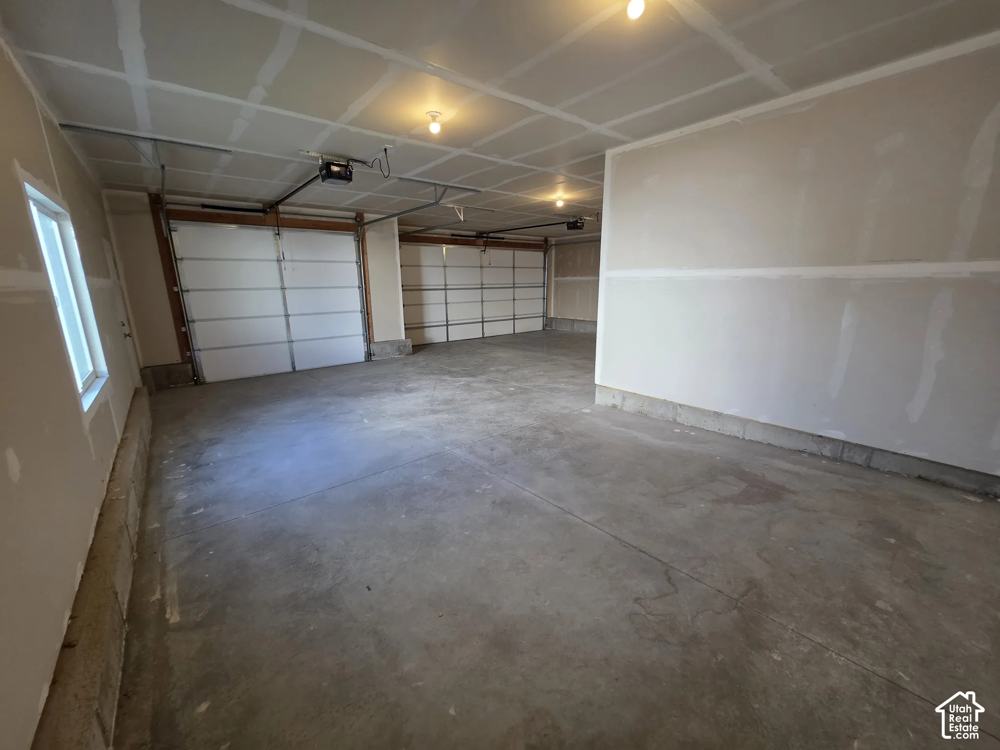 Three-car garage with concrete flooring, two overhead garage doors, and a single window