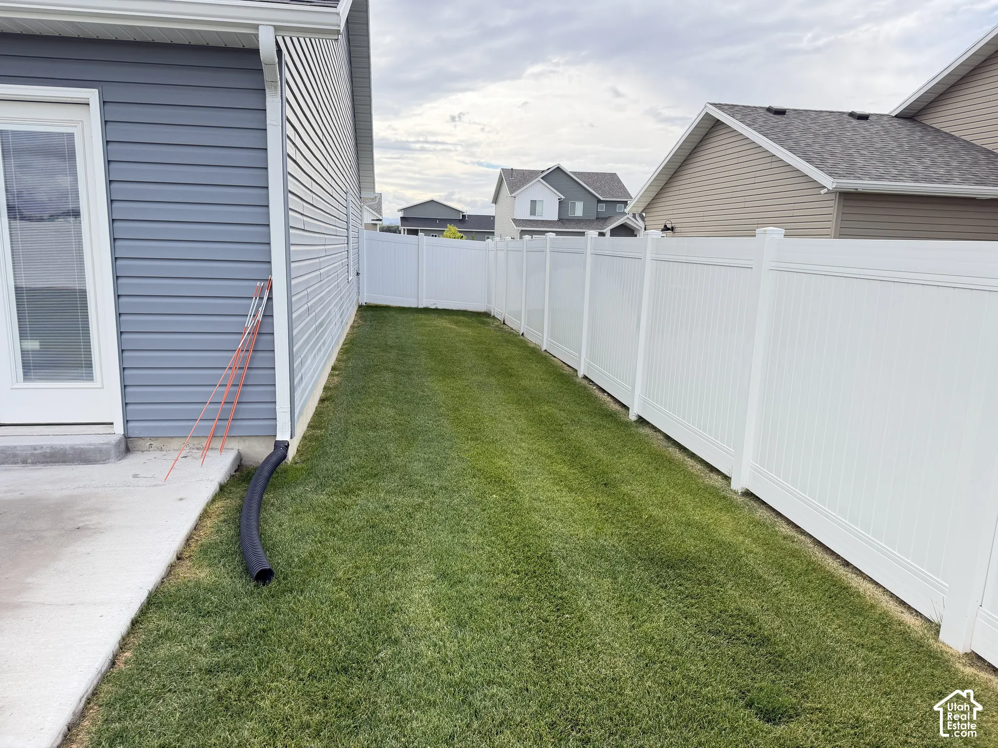 White vinyl fencing enclosing a grass lawn with a concrete patio and a siding exterior