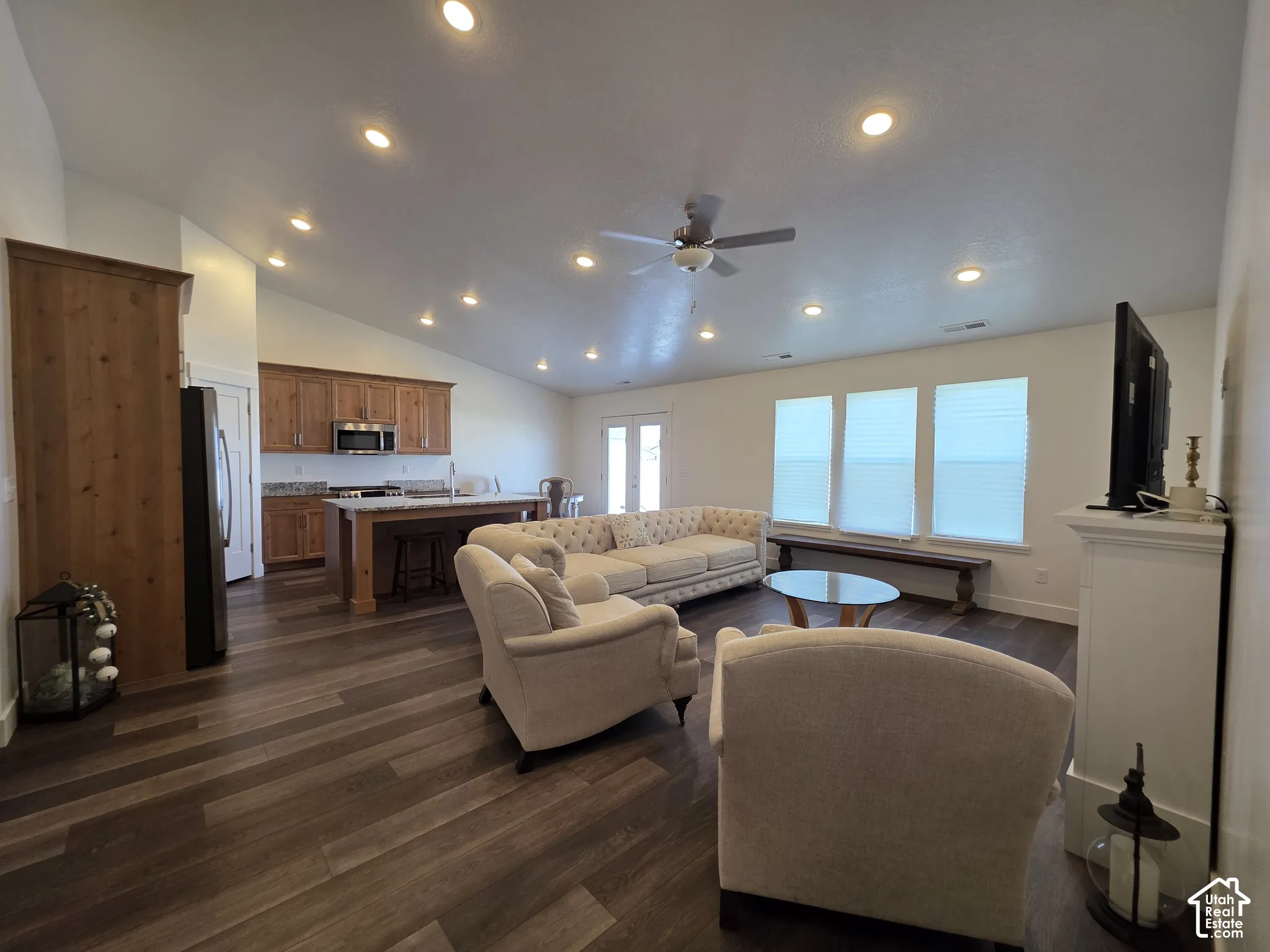 Open-concept living space featuring wood-finish flooring, vaulted ceilings with recessed lighting, and a kitchen island with seating