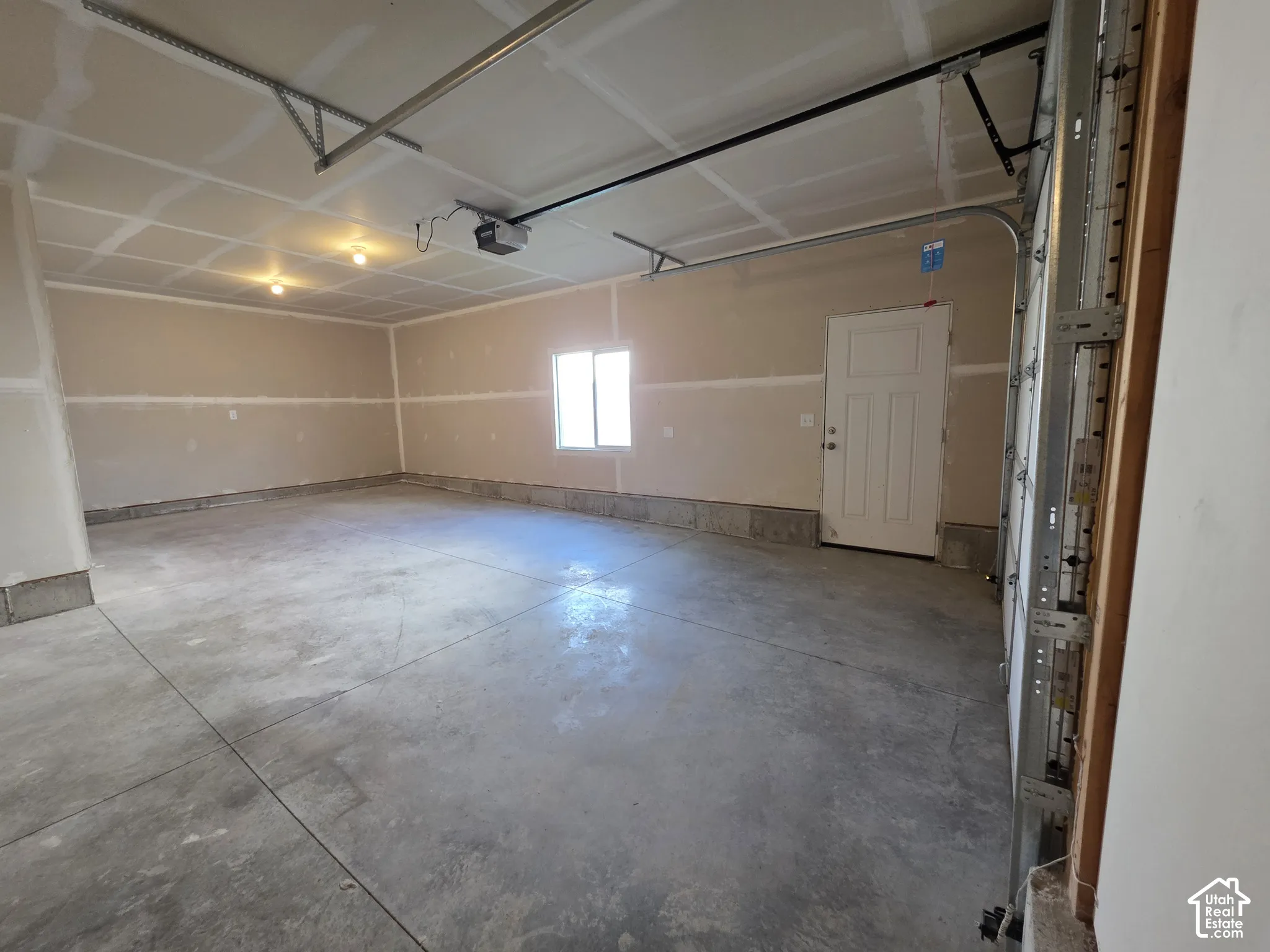 Spacious garage with concrete flooring, finished drywall, overhead lighting, and an automatic garage door opener