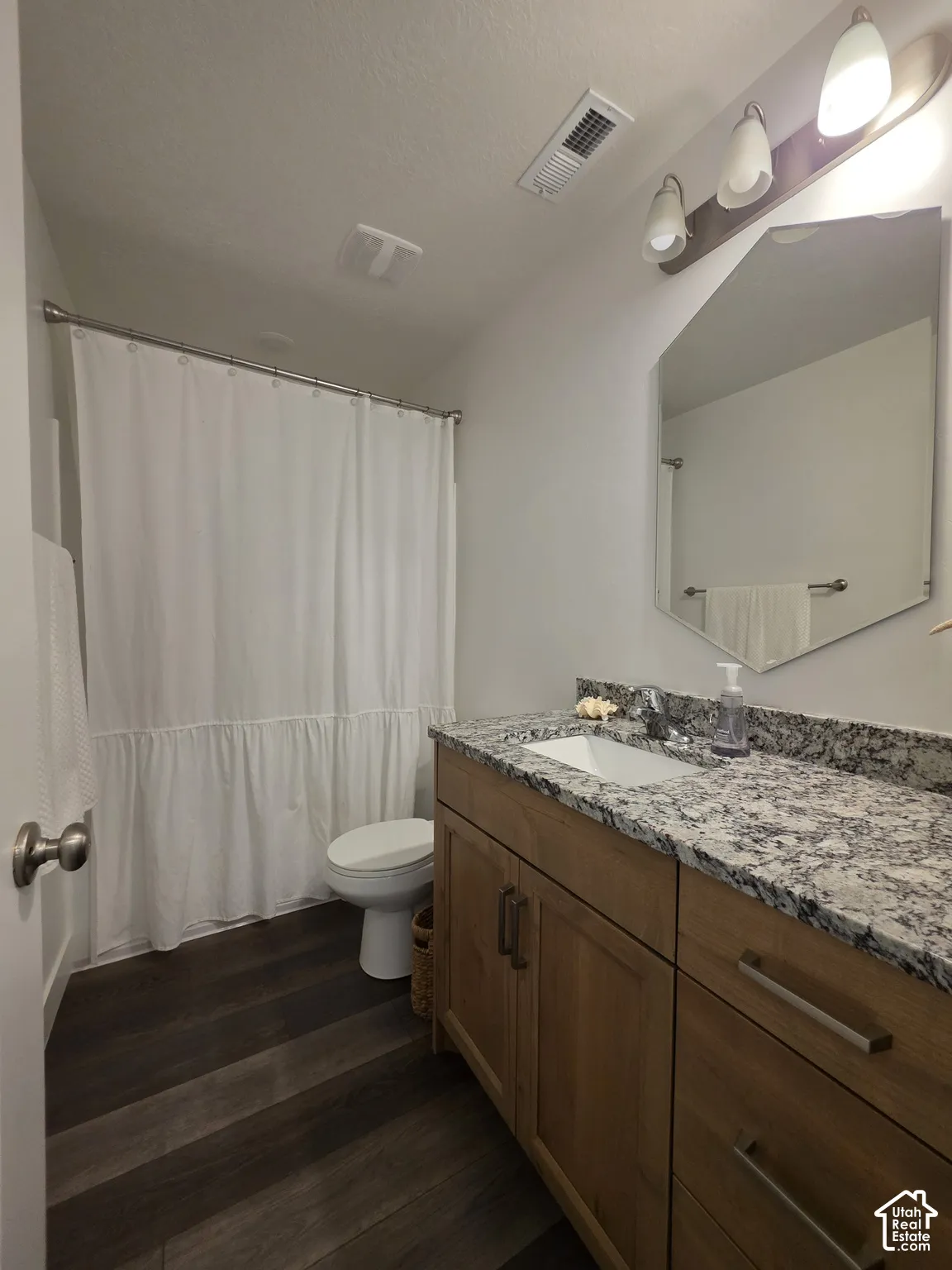 Bathroom featuring a wood-finish vanity with an integrated sink, stone countertop, and dark wood-finish flooring