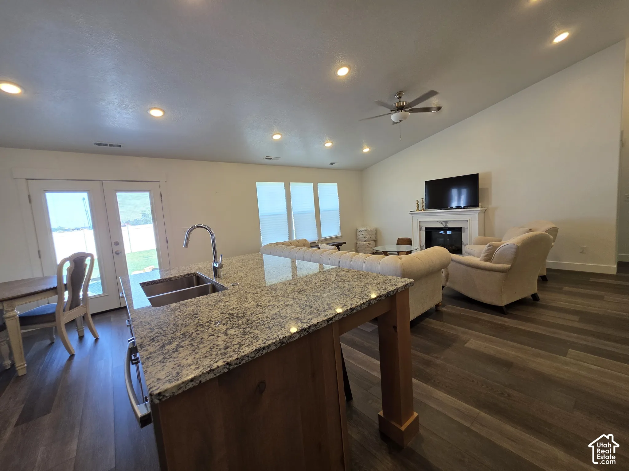 Spacious living area featuring a kitchen island with stone-finish countertop and double basin sink, LVP flooring, recessed lighting, and a vaulted ceiling with a ceiling fan
