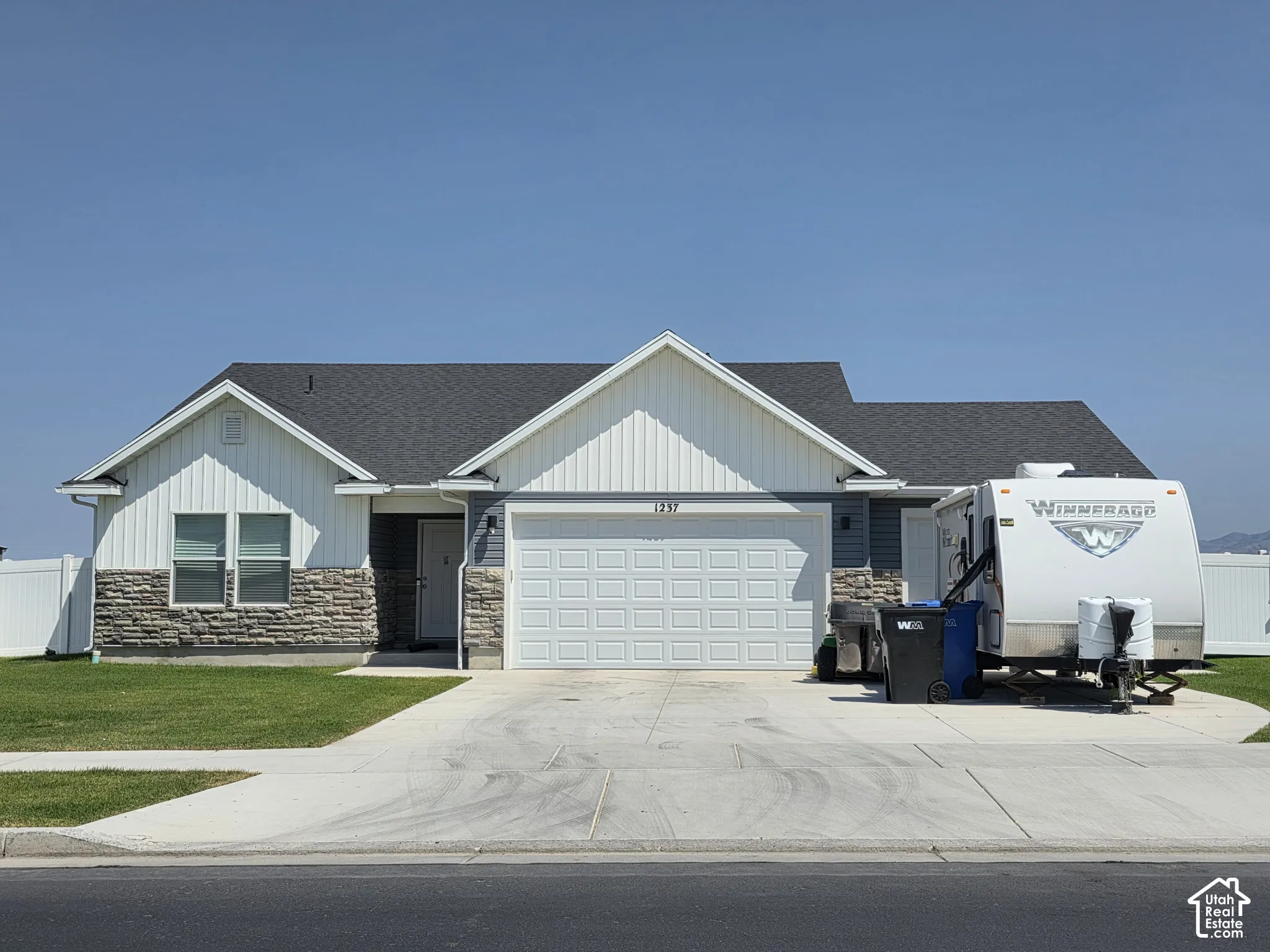 Modern ranch-style residence featuring a gray shingle roof, white vertical siding, and stone facade accents