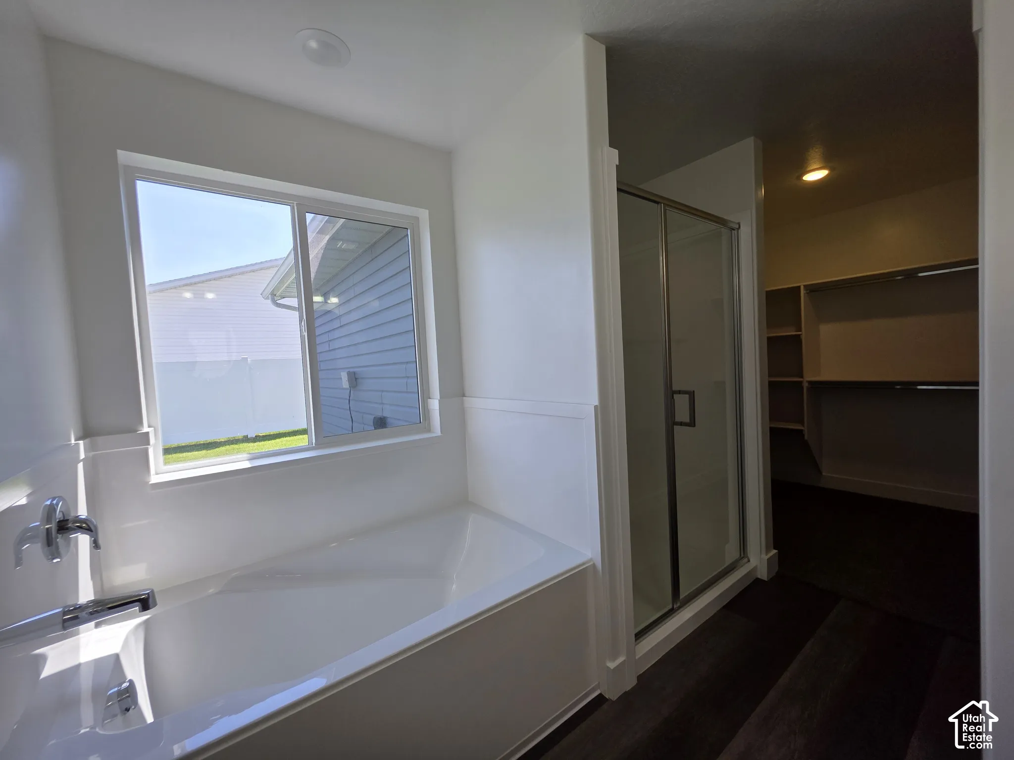 Bathroom featuring a white soaking tub with polished chrome fixtures, a clear glass enclosed shower, and dark wood-finish flooring