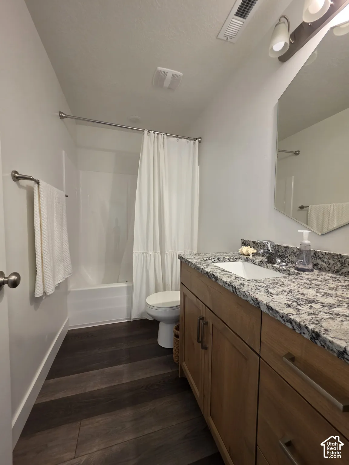 Bathroom featuring a wood-finish floor, a light wood vanity with an integrated sink, a speckled countertop, and a shower-over-tub combination
