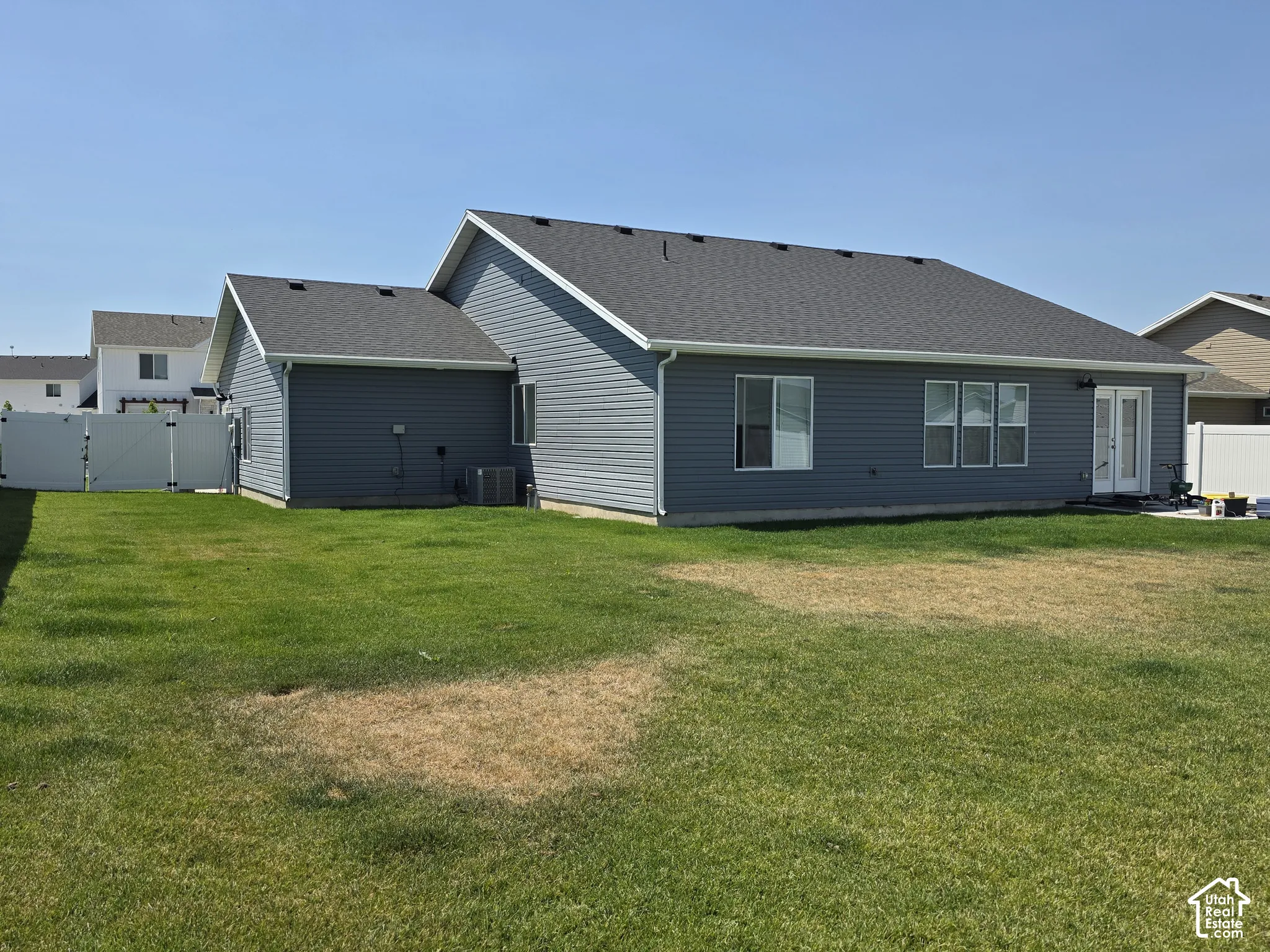 Rear exterior featuring dark gray siding, a charcoal shingle roof, and white vinyl fencing