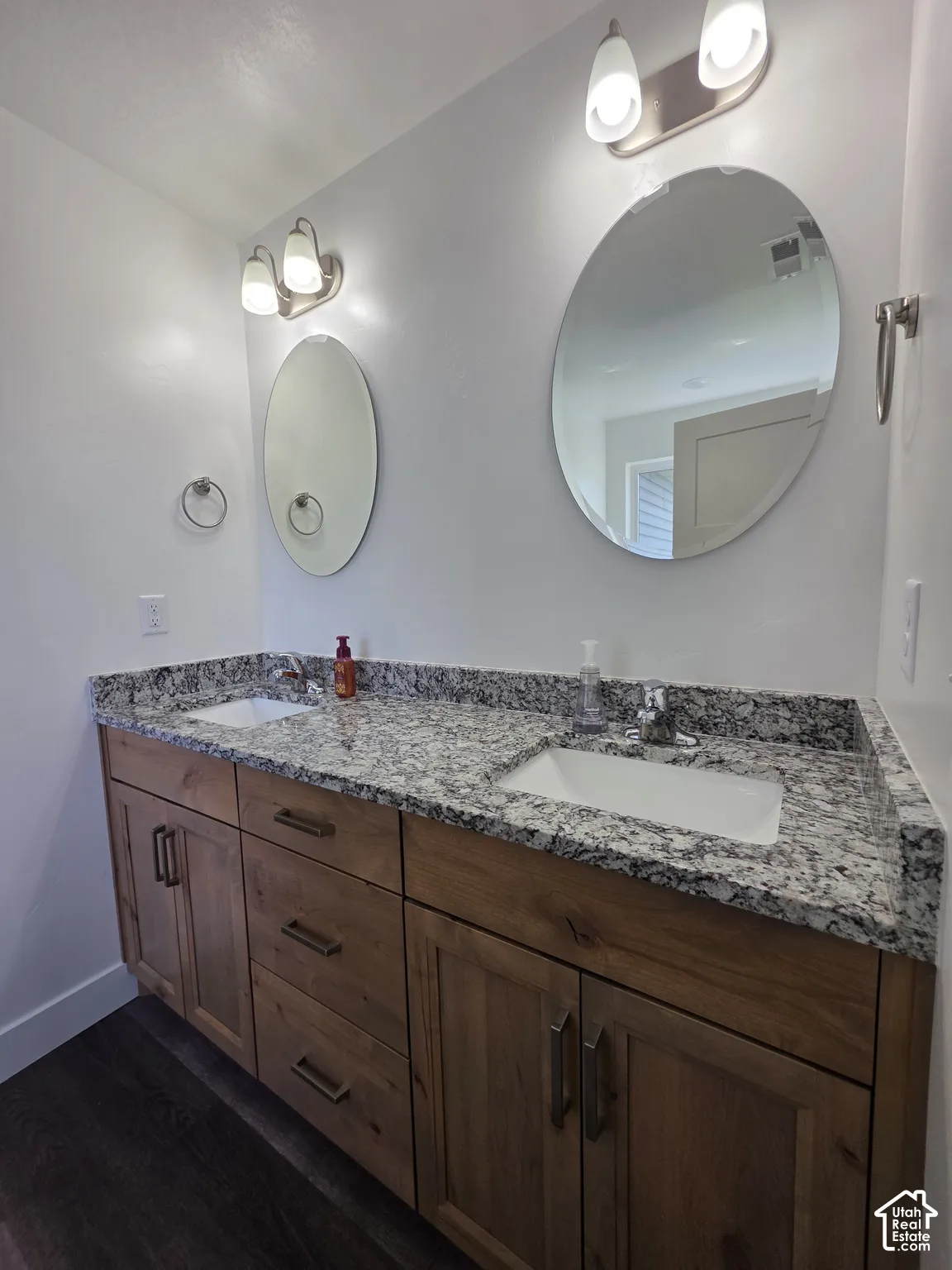 Dual vanity featuring a granite countertop with integrated sinks, wood-finish cabinetry, and contemporary lighting fixtures