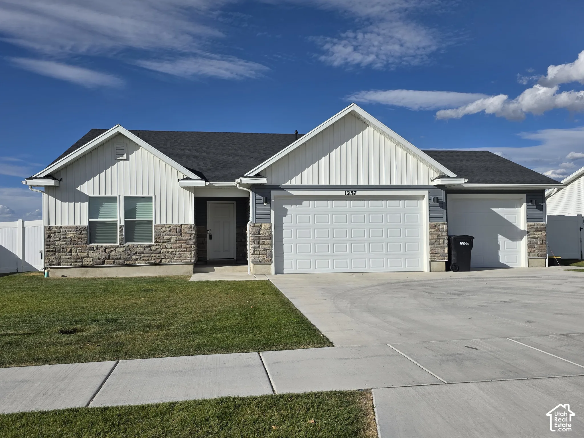 White vertical siding and grey horizontal siding exterior with stone veneer accents, a dark shingled roof, an attached two-car garage, and concrete driveway