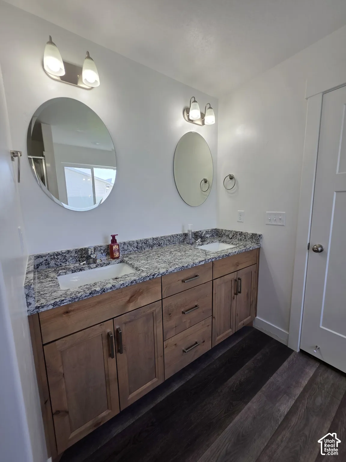 Double vanity featuring wood-finish cabinetry, under-mount sinks, and speckled countertops