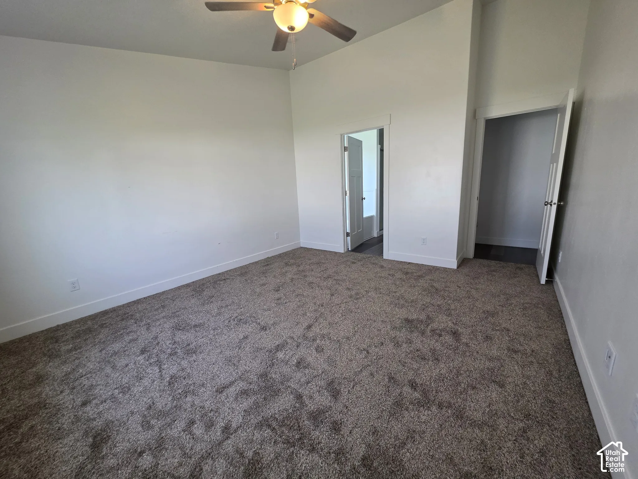 Spacious bedroom with neutral wall finishes, carpeted flooring, ceiling fan with integrated lighting, and dual closet access including a mirrored sliding door option